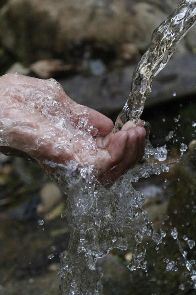 Hands collecting clean off-grid water from a natural spring outdoors