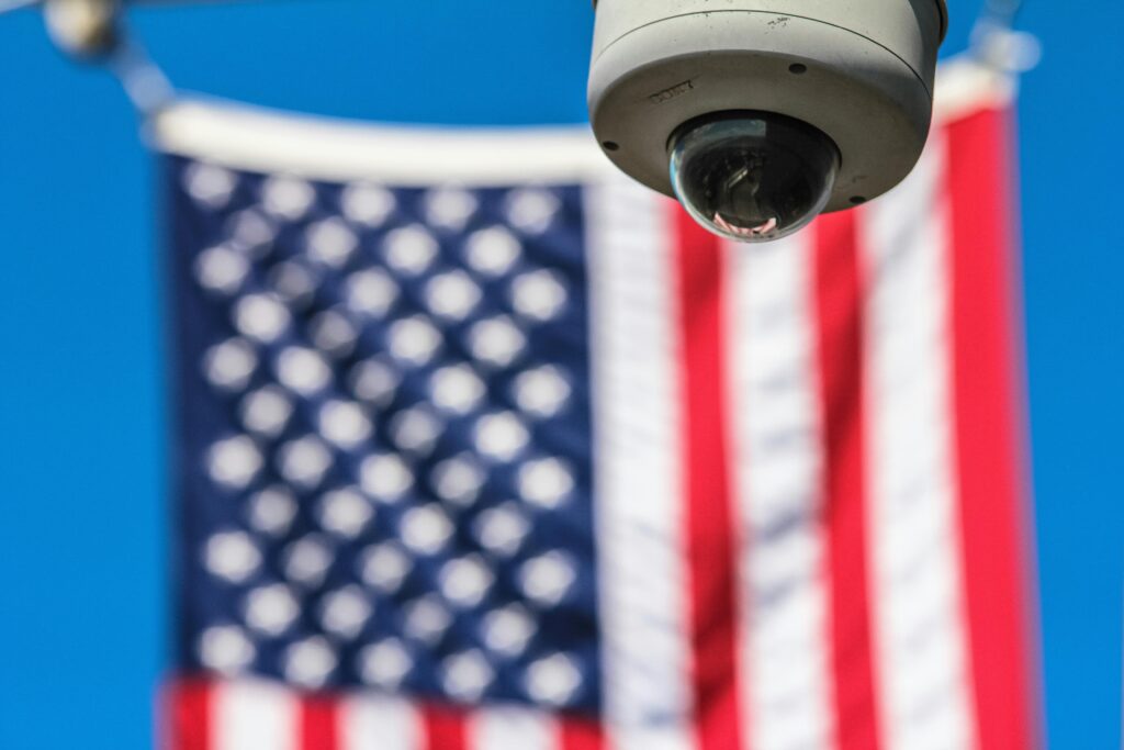Surveillance camera watching American flag — symbolic image of a technological police state